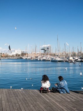 İki kadın turist eski limanda martılarla çevrili dinleniyor. 