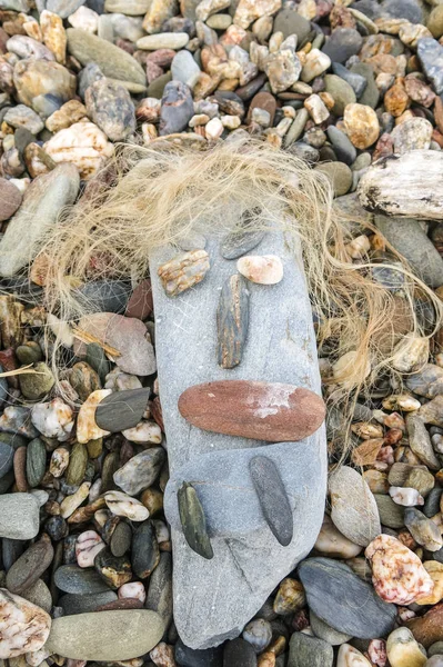 Простое лицо, созданное на пляже с небольшими камнями и сушеным водорослем — стоковое фото