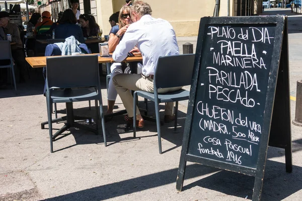 Tourists eat in the Barceloneta, the seaside neighborhood of Barcelona. The board announces "seafood paella, grilled fish and veal steak" — Φωτογραφία Αρχείου