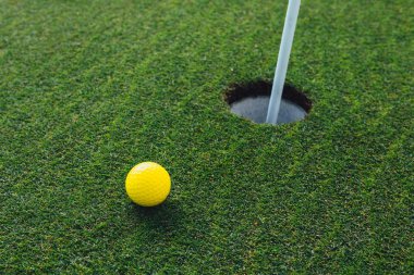 sarı golf topu yakın PIN bayrak, yeşil çim arka plan, closeup görünümü ile delik