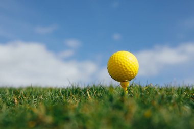 tee, yeşil çim ve mavi gökyüzü arka plan üzerinde sarı golf topu