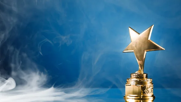 Guld stjärna trophy i rök, blå bakgrund — Stockfoto