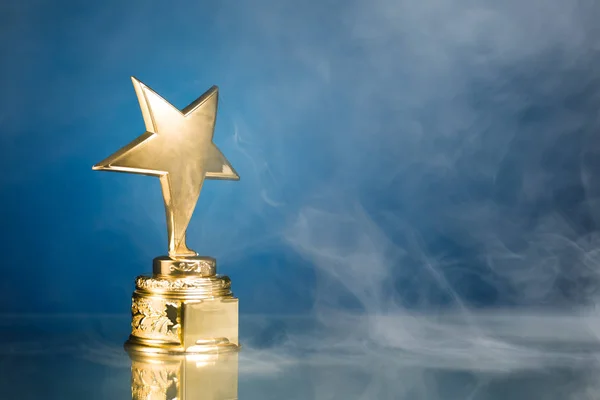 Gold star trophy in smoke, blue background — Stock Photo, Image