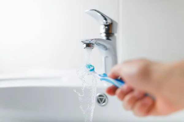 Hand holding toothbrush under flowing water from faucet — Stock Photo, Image