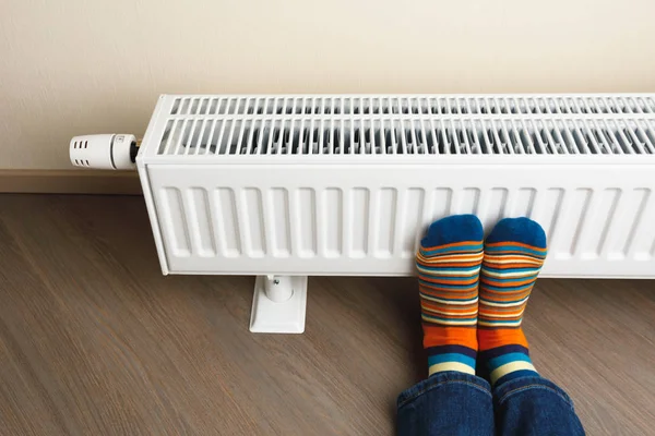 Pernas com meias coloridas na frente do radiador de aquecimento — Fotografia de Stock