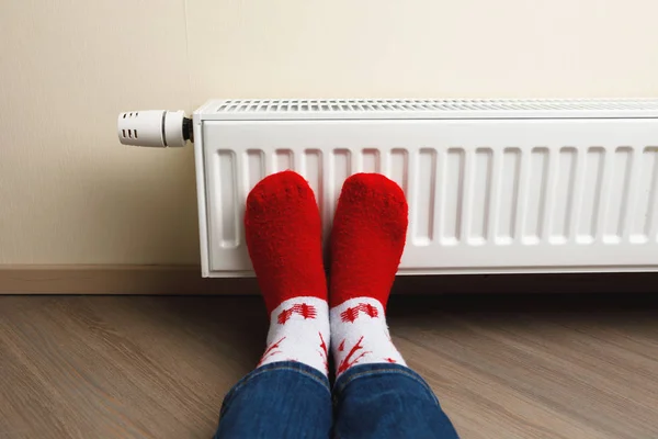 Gambe con calzini di cervo rosso di Natale davanti al radiatore di riscaldamento — Foto Stock