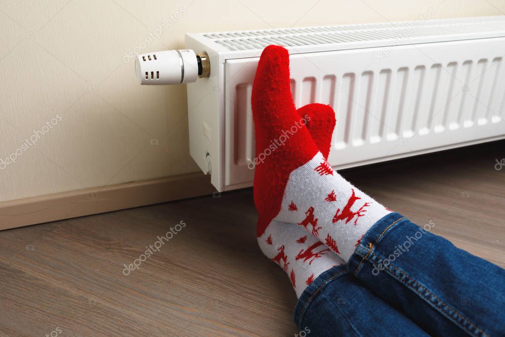 legs with red Christmas deer socks in front of heating radiator