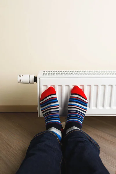 Jambes avec des chaussettes colorées devant le radiateur de chauffage — Photo