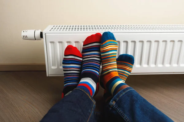 Gambe con calzini colorati davanti al radiatore di riscaldamento — Foto Stock