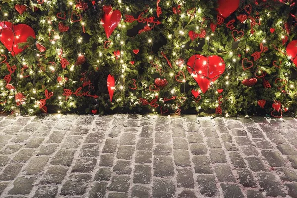 Fundo de Natal com luzes no pinheiro, corações de amor vermelho e pavimentação de pedra — Fotografia de Stock