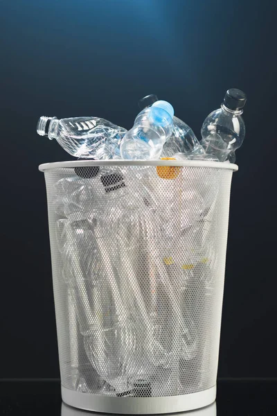Bidone della spazzatura con bottiglie di plastica sprecata, sfondo nero — Foto Stock