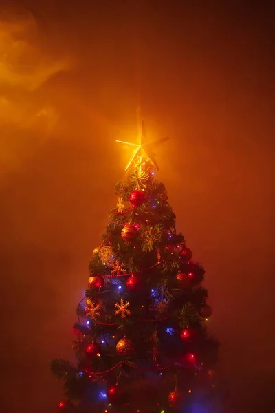 Рождественская елка с праздничными огнями, оранжевый фон с дымом — стоковое фото