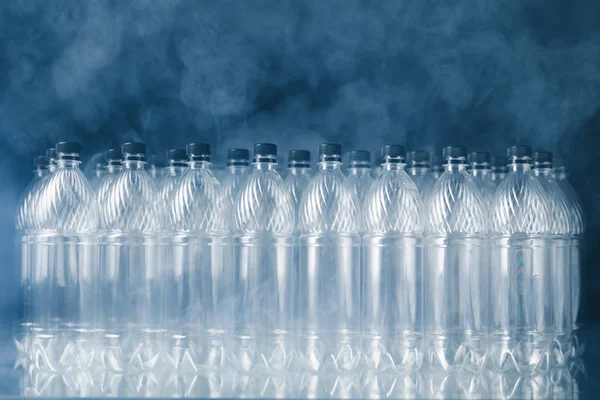 Пустые пластиковые бутылки на черном фоне с дымом, концепция загрязнения — стоковое фото