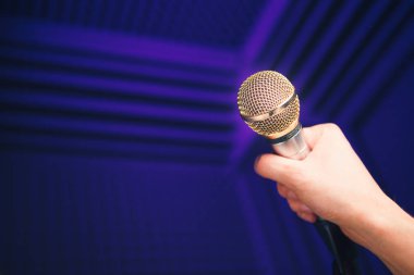 Elinde altın mikrofon, stüdyoda akustik köpükle mor arka plan