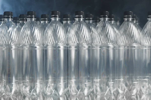 Пустые пластиковые бутылки на черном фоне с дымом, концепция загрязнения — стоковое фото