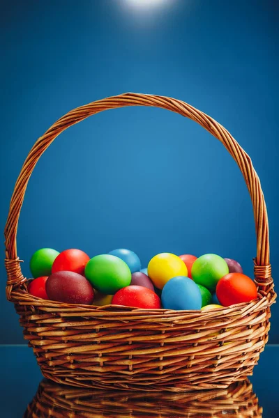 Easter color eggs in festive gift basket, blue background with copy-space