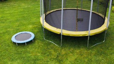 small trampoline near big one with round mat, size comparison, green lawn background clipart