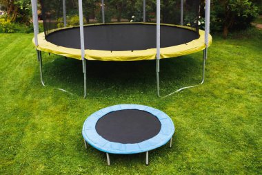 small trampoline near big one with round mat, size comparison, green lawn background clipart