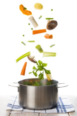 Fresh vegetables to cook a soup falling into a pot isolated on a white background clipart