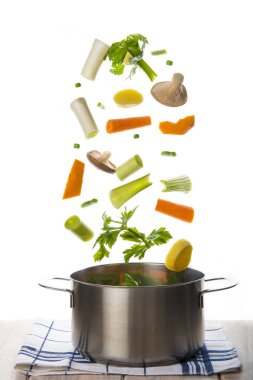 Fresh vegetables to cook a soup falling into a pot isolated on a white background clipart