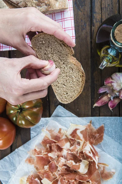 Chef rubbing garlic on a bread slice to prepare ham with garlic, tomato bread and olive oil Spanish style