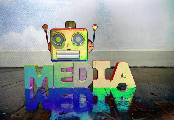 red robot head on wooden letters that say MEDIA   on an old wooden floor