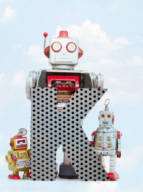 mavi gökyüzü ile büyük bir metal harf K tutan retro robotlar 