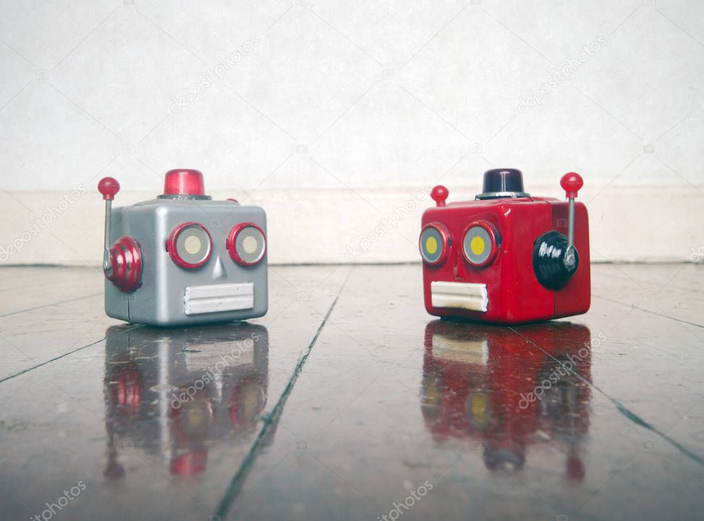 two metal robot heads chatting on a wooden floor
