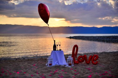 Gün batımında sahilde şarap kadehleri, balon, lambalar ve aşk balonu. Aşk ve aşk teması
