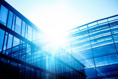 Mavi gökyüzünde güneş ışınları ile gökdelen cam cepheler. Modern binalar