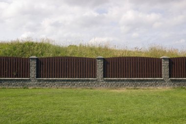 Uzun onew katı kahverengi ahşap kırsal çit üzerinden dikey Çam kalas. Gri tuğladan yapılmış Bankası. Güneşli yaz gün kırsal çimenli manzara