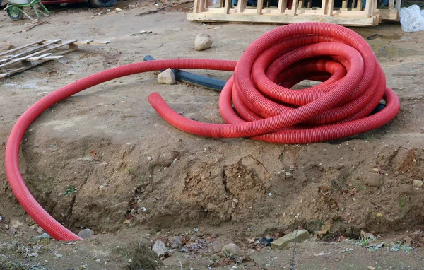 Red armed plastic pipes for a drainage and melioration lie on a city construction site. Mass production