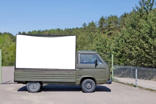 An old green army truck with a billboard set in a forest recreat