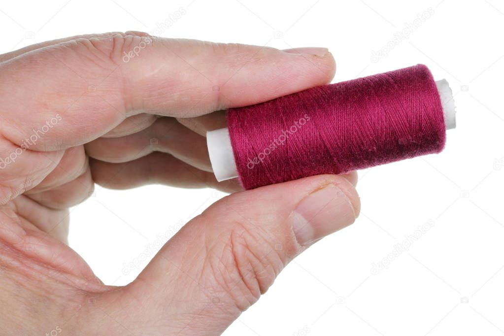 An elderly male tailor holds a bobbin of red thread in his hand 