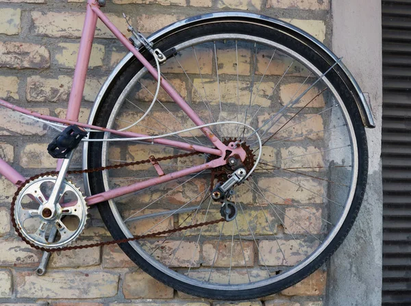 黄色のレンガの壁にかかって壊れたピンクのレトロな自転車の車輪 — ストック写真