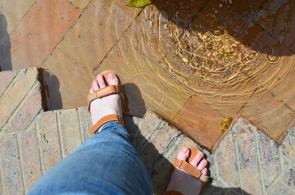 Women\'s feet in sandals and the old city fountain