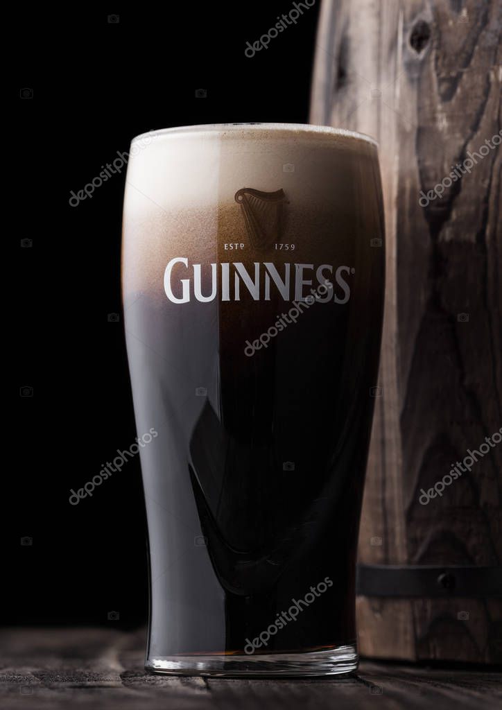 LONDON, UK - APRIL 27, 2018: Original glass of Guinness draught stout beer  next to old wooden barrel. Guinness beer has been produced since 1759 in Dublin, Ireland.