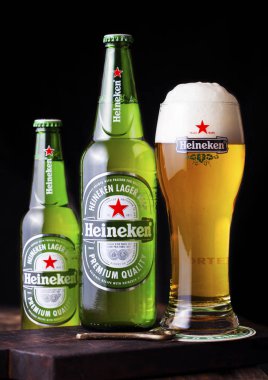 LONDON, İngiltere - 27 Nisan 2018: Koyu ahşap arka planda Heineken Bira şişeleri ve orijinal cam. Heineken, Heineken Enternasyonal 'ın sancak gemisi.