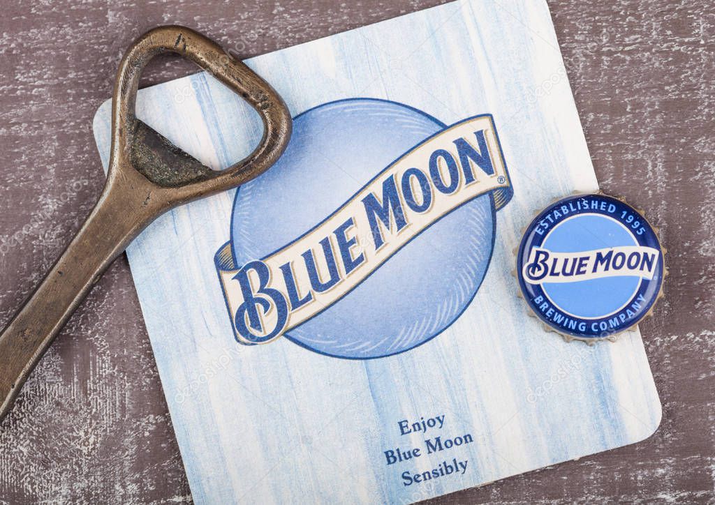 LONDON, UK - AUGUST 10, 2018:Blue Moon beer coaster with bottle top and opener on wooden background.
