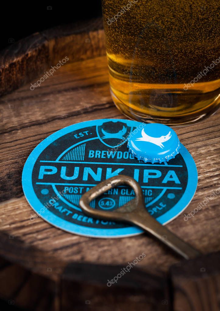 LONDON, UK - AUGUST 10, 2018: Brewdog Punk Ipa beer coaster with bottle top and opener and glass of beer on top of wood barrel.