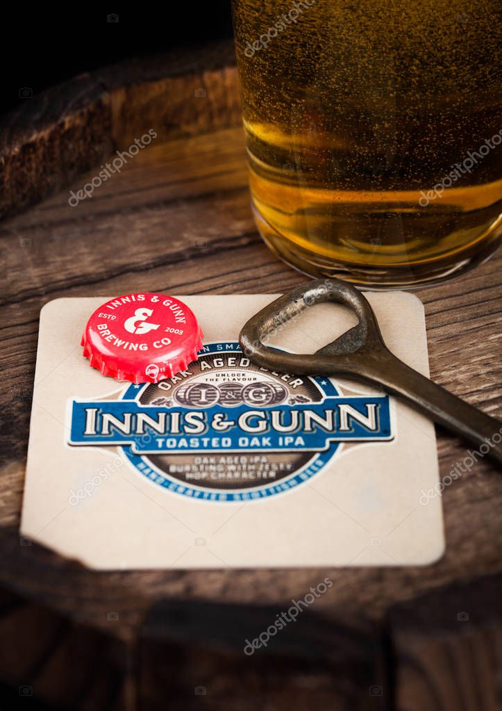 LONDON, UK - AUGUST 10, 2018: Innis & Gunn beer coaster with bottle top and opener and glass of beer on top of wood barrel.
