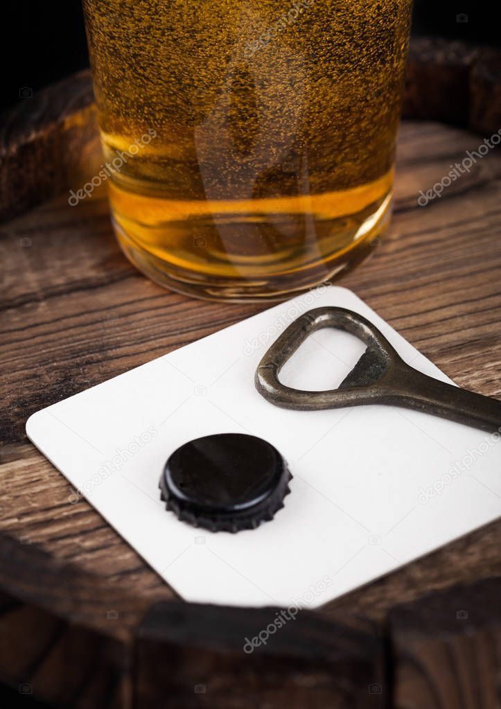 Beer coaster with bottle top and opener and glass of beer on top of wood barrel.