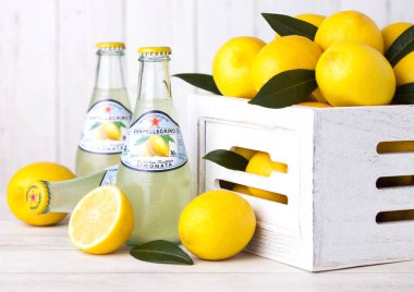 LONDON, UK - SEPTEMBER 03, 2018: Glass bottles of San Pellegrino sparkling lemon soda drink on wooden background with fresh lemons in white box. clipart
