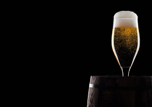 Cold glass of craft beer on old wooden barrel on black background with dew and bubbles. With space for your text.