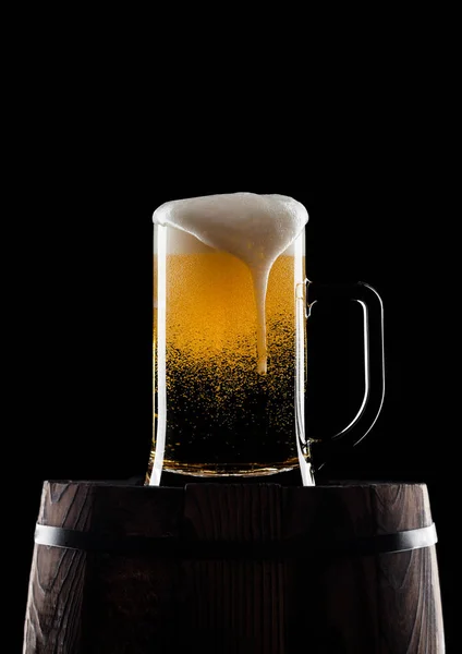 Cold glass of craft beer on old wooden barrel on black background with dew and bubbles