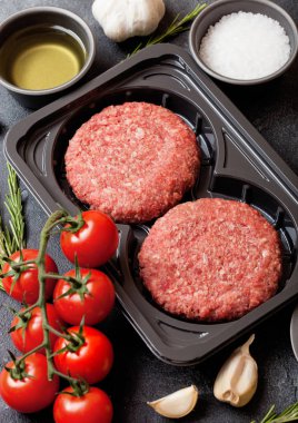 Plastik tepsi ile baharat ve otlar ile çiğ kıyılmış ev yapımı ızgara sığır eti hamburger. Üstten görünüm ve metin için yer.