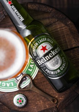 LONDON, İngiltere - 27 Nisan 2018: Orijinal cam ve şişe Heineken Lager Birası bardak altlığı ve şişe açacağı ile eski ahşap fıçının üzerinde. Heineken, Heineken Enternasyonal 'ın sancak gemisi.