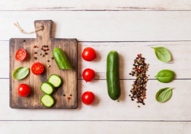 Organik domates ve salatalık Doğrama Kurulu ahşap mutfak masasında üzerinde fesleğen ve keten havlu ile.