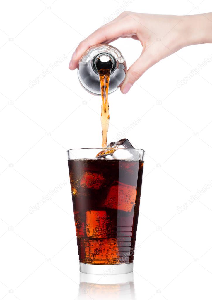 Female hand pouring cola soda drink from bottle to glass  with ice cubes on white background