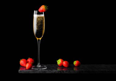 Zarif bir bardak sarı şampanya üzerinde çilek ve siyah mermer tahtada taze böğürtlen..